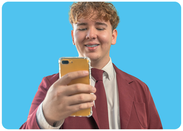 Joven sonriente con un traje bordó mirando su smartphone sobre un fondo azul.